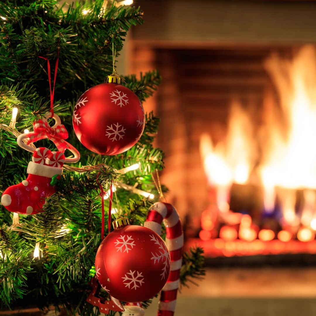 Cozy ambiance with decorated Christmas tree in front of a wood fireplace.